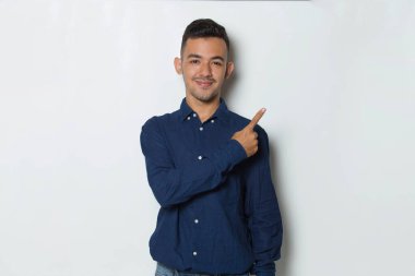 Genç yakışıklı iş adamı beyaz arka planda izole edilmiş boş alanı işaret ediyor.