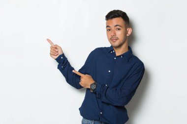 Genç yakışıklı iş adamı beyaz arka planda izole edilmiş boş alanı işaret ediyor.