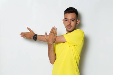Sarı tişörtlü genç adam beyaz arka planda esneme hareketleri yapıyor.