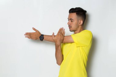 Sarı tişörtlü genç adam beyaz arka planda esneme hareketleri yapıyor.