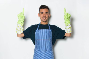 Önlük takan temizlikçi ve eldivenler, beyaz arka planda, el ve parmaklarıyla işaret ediyor.