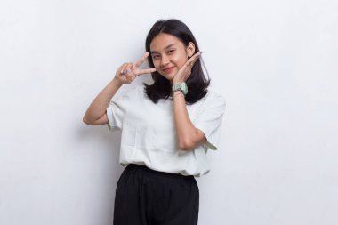 Güzel genç Asyalı kız beyaz arka planda barış ya da zafer işareti gösteriyor.