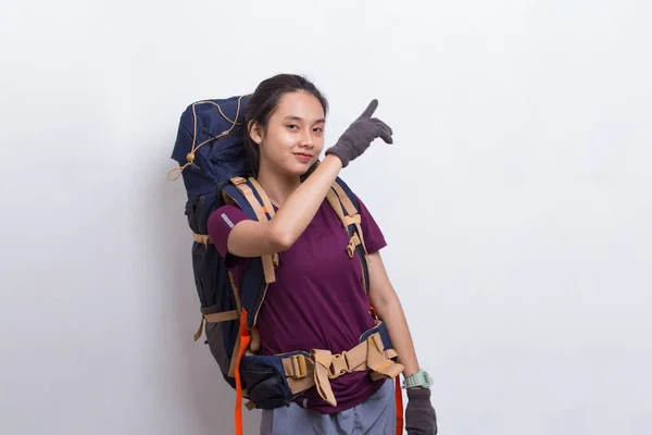 Young asian hiker woman with backpack pointing finger on empty space on white background