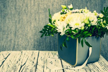 Ahşap bir platformdaki bir kutunun içindeki çiçeklerin kompozisyonu ve gri bir arkaplan