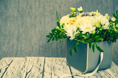 Ahşap bir platformdaki bir kutunun içindeki çiçeklerin kompozisyonu ve gri bir arkaplan