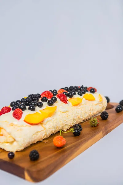 Meringue roll side view at an angle, on a white background, close-up, wooden board decorated with fruit