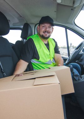 Delivery boy smiles at the camera inside his van.