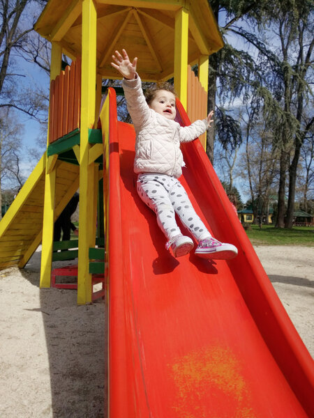 Excited little girl sliding down a slide 
