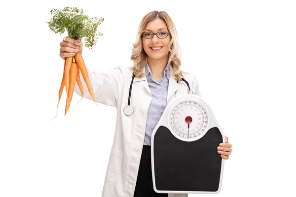女医生抱着胡萝卜和体重秤 — 图库照片