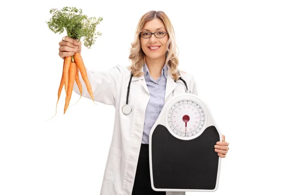 Doctora sosteniendo zanahorias y una báscula de peso —  Fotos de Stock