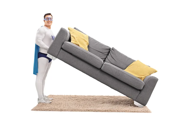 ソファーを持ち上げるスーパー ヒーローの衣装の男 — ストック写真