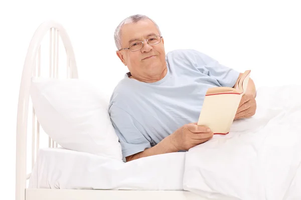 Senior man in bed een boek houden — Stockfoto