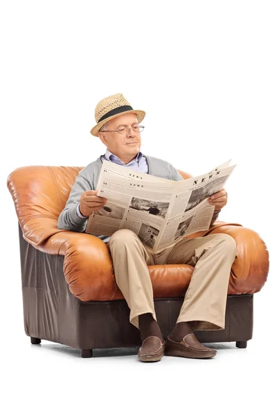 Senior czytanie gazety w pozycji siedzącej na fotelu — Zdjęcie stockowe