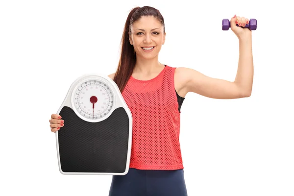 Woman holding dumbbell and weigh scale — Stock Photo, Image