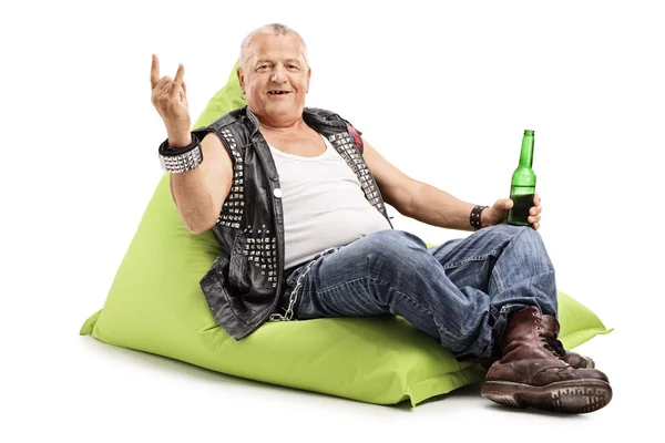 Зрелый панк пьет пиво, сидя на бобовом мешке. — стоковое фото