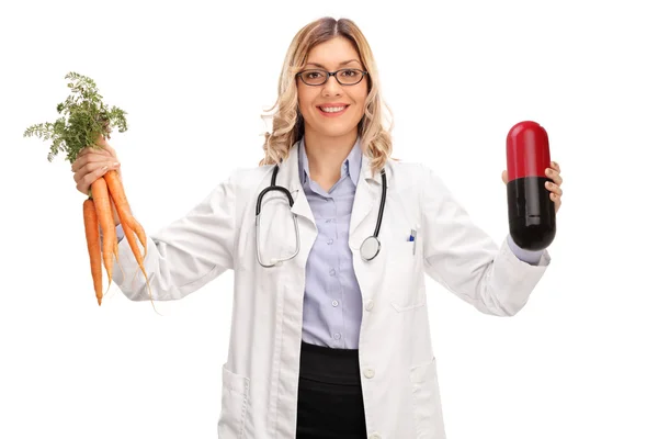 Médico femenino sosteniendo una píldora enorme y zanahorias — Foto de Stock