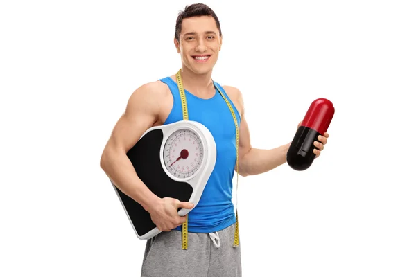 Guy holding a huge pill and a weight scale — Stock Photo, Image