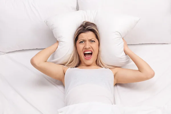 Furious woman covering ears with pillow — Stock Photo, Image