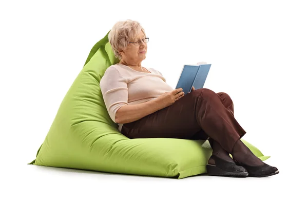 Mature lady reading book seated on beanbag — Stock Photo, Image