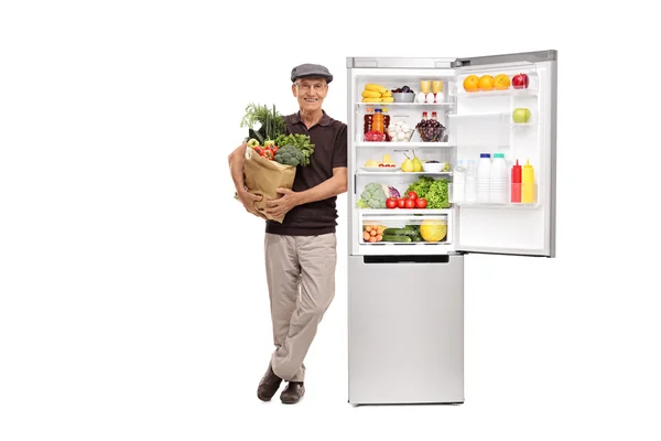 Senior man holding groceries by a fridge — Stock Photo, Image