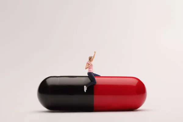 Delighted woman sitting on a giant pill — Stock Photo, Image