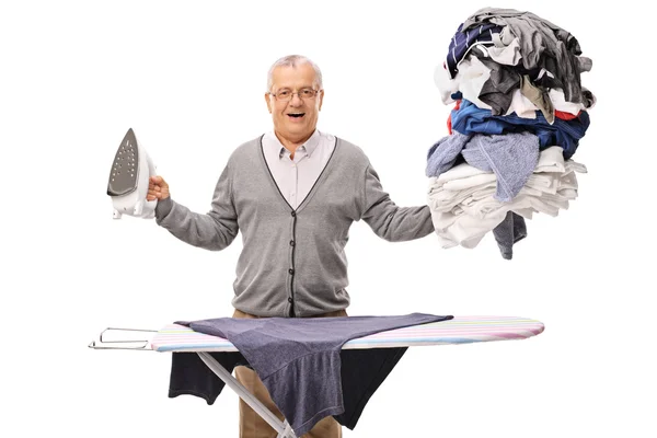 Senior man ironing a pile of clothes — Stock Photo, Image