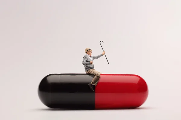 Mature man sitting on a giant pill — Stock Photo, Image