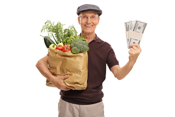 Elderly man holding a bag of groceries and money — Stock Photo, Image