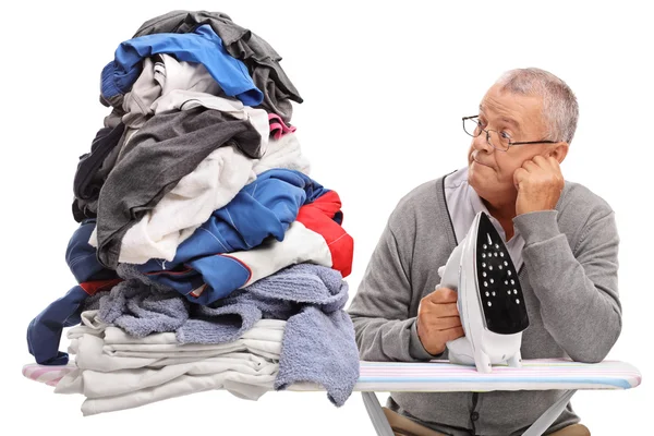 Uomo in possesso di un ferro da stiro e guardando mucchio di vestiti — Foto Stock