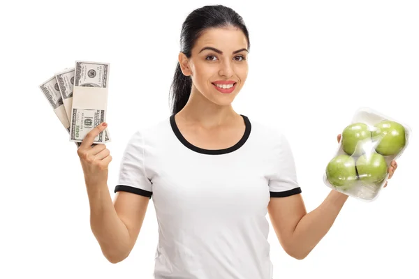 Mujer sosteniendo manzanas y montones de dinero — Foto de Stock