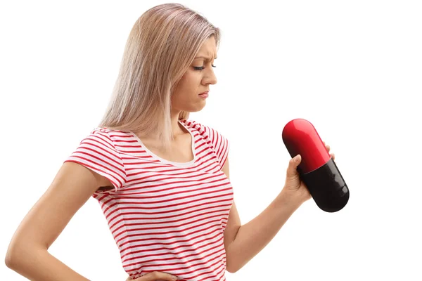 Sad young woman looking at a big pill — Stock Photo, Image