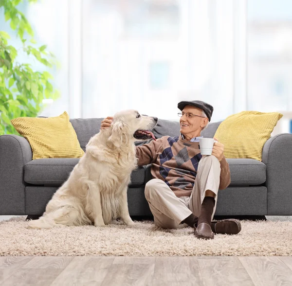 Elderly man sitting on the floor and petting his dog — Stock Photo, Image