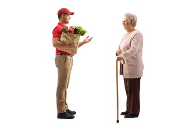 Elinde market poşeti olan bir teslimatçının beyaz arka planda izole edilmiş yaşlı bir kadınla konuşurken tam boy profil fotoğrafı.
