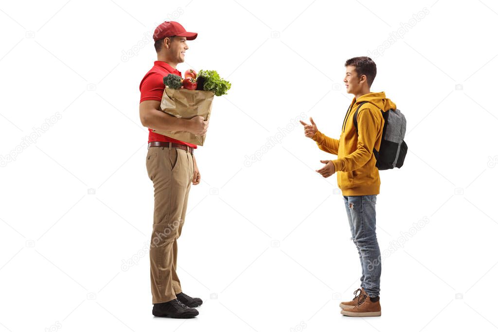 Full length profile shot of a guy delivering a grocery bag to a teenage schoolboy isolated on white background