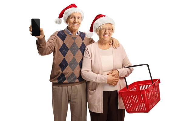陽気高齢者のカップルでクリスマスのサンタの帽子と白い背景に隔離された空のショッピングバスケット — ストック写真