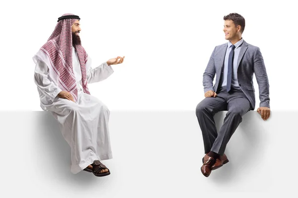 Saudita Thobe Sentado Painel Branco Falando Com Homem Terno Isolado — Fotografia de Stock