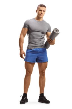 Spor kıyafetli genç bir adamın beyaz arka planda izole edilmiş egzersiz paspası tutarken tam boy portresi.