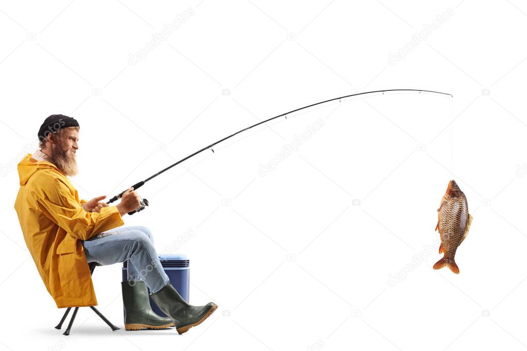 Full length profile shot of a young fisherman sitting on a chair and catching fish isolated on white background