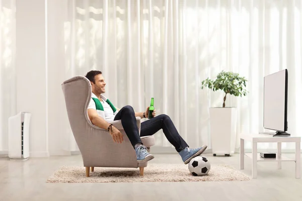 一个戴着围巾和啤酒的家伙坐在扶手椅上 在家里看电视上的足球比赛 — 图库照片