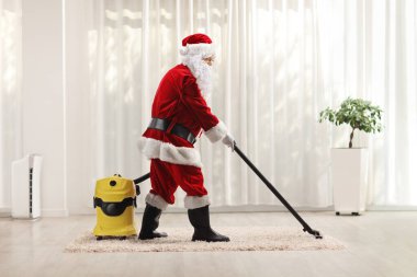 Noel Baba evde elektrikli süpürge kullanıyor.