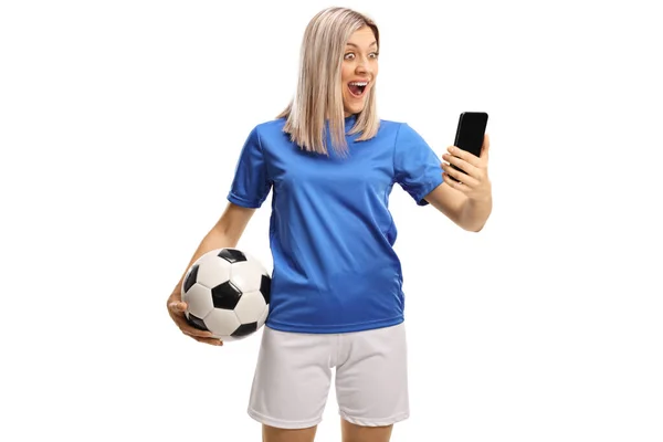 サッカーボールを持つ驚きの女性サッカー選手と白い背景に隔離されたスマートフォン — ストック写真