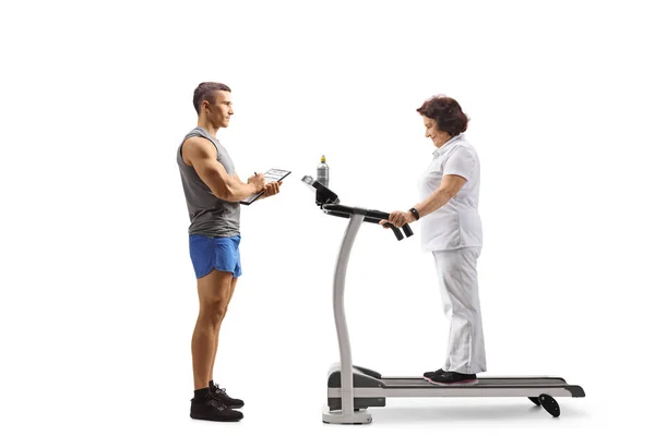 一名健身教练和一名老年妇女在白色背景隔离的跑步机上拍摄的全长轮廓 — 图库照片