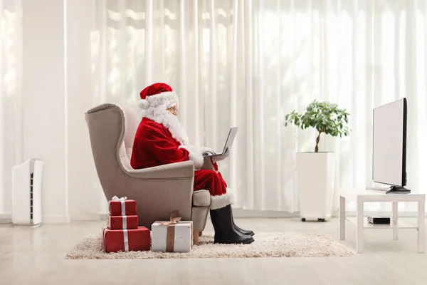 Santa Claus Arbetar Bärbar Dator Och Sitter Fåtölj Ett Vardagsrum — Stockfoto