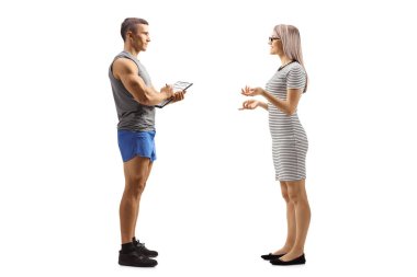 Beyaz arka planda izole edilmiş bir fitness eğitmeniyle konuşan genç bir kadının tam boy profil çekimi.