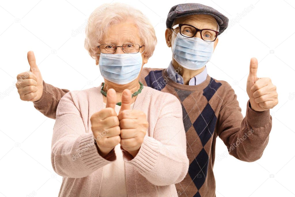 Elderly man and woman with protective face masks showing thumbs up isolated on white background