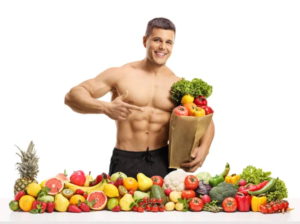 赤裸裸的英俊男子 提着一袋食品和一堆白色背景的水果蔬菜 — 图库照片
