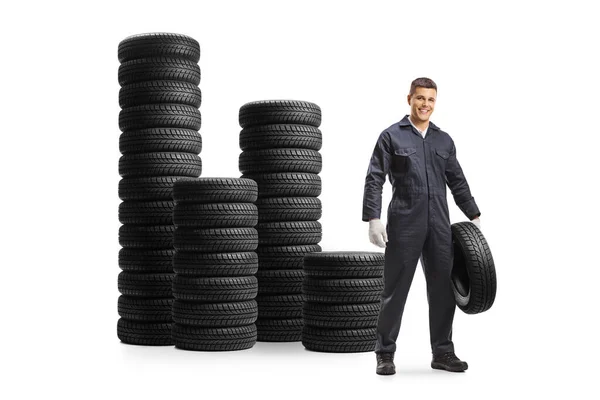 タイヤの山と白い背景に隔離された車のタイヤを保持する自動車整備士 — ストック写真