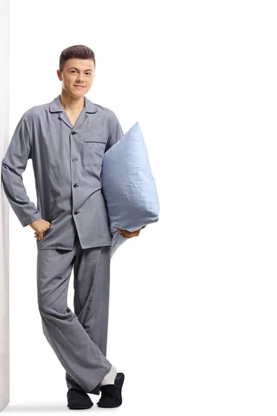 壁に寄りかかって白い背景に孤立した枕を持っているパジャマ姿の若い男の完全な長さの肖像画 — ストック写真