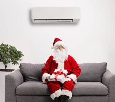 Noel Baba bir kanepede oturuyor ve duvarında bir klima var.