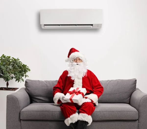 Santa Claus Sedí Pohovce Dárkem Pod Klimatizací Připevněnou Stěně — Stock fotografie